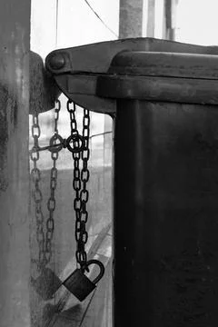 Locked trash can chained to wall in urban setting during daylight hours Stock Photos