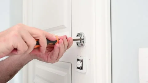 A locksmith adjusts the door handle of a modern white interior door Stock Footage 290043552