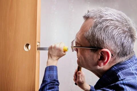 Locksmith fits new lock by chiseling rectangular mortise for latch plate in.. Stock Photos