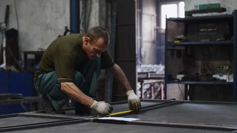 Locksmith measures tape measure length of metal bars and makes marks in workshop Stock Footage 112859437