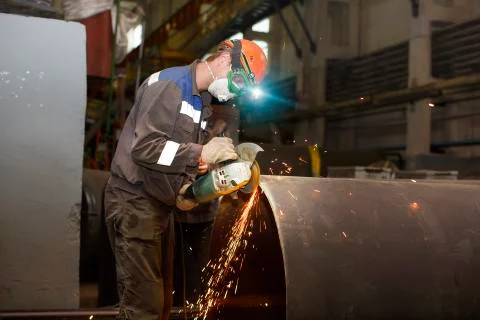 Locksmith processes pipe edge with electric hand grinder Stock Photos