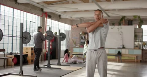 Loft gym members warming up before lifting while gray-clad man stretching Stock Footage 337286728