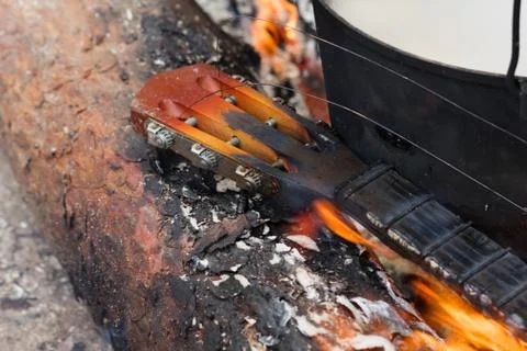 Log of pine tree, burning neck of guitar and old sooty cauldron on bonfire Foto stock