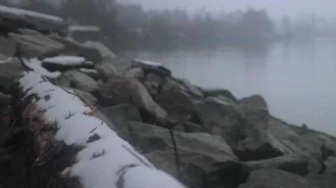 A log with snow falling on it by the side of the river Stock Footage 59140695