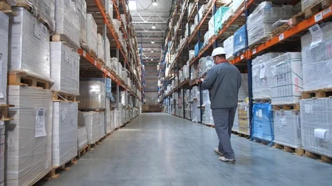 Logistics warehouse. The worker goes between the stands with the pack and makes Video stock 111764502