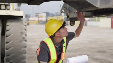 Logistics worker in a hard hat inspects heavy machinery at a container port Stock Footage 334947170