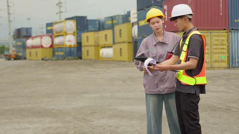 Logistics workers collaborate while reviewing documents at a busy container yard Stock Footage 346078069