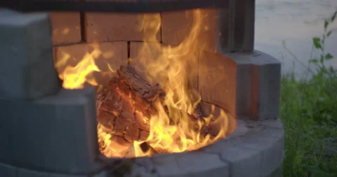 Logs burning in campfire pit by the lake at evening in slow motion Vídeo Stock 130927610
