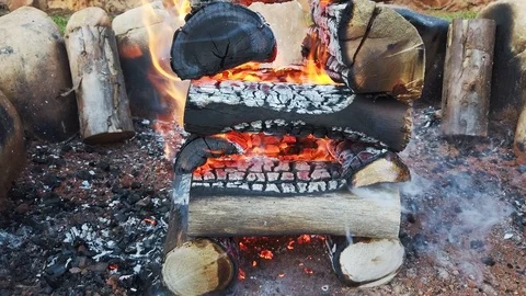 Logs stacked in a log-cabin style in a fire pit while flames burn the wood. Stock Footage 109273371