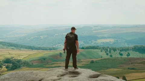 Lone backpacker walking toward cliff edge above sweeping mountain valley and Stock Footage 344867958