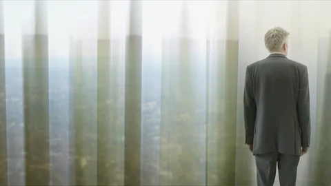 Lone businessman looking through curtains to city behind Video stock 89902053