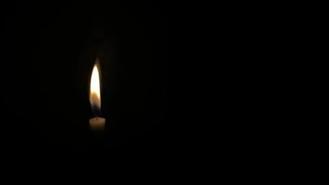 A lone candle flame flickering gently against a completely dark backdrop. Stock Photos