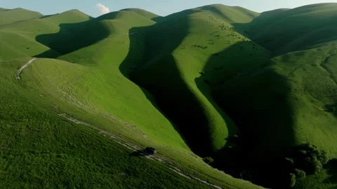 A lone car navigates through the rugged terrain of a lush green hill, surrounded Stock Footage 257513523