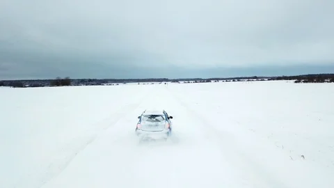 A lone car rides on a snowy road in a white field. The drone follows the car Stock Footage 101714863