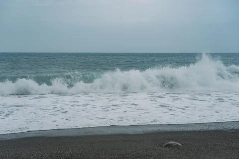 Lone crashing wave on black rocky beachfront. Stock Photos