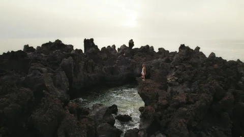 A lone explorer stands atop sharp cliffs overlooking tranquil ocean waters below Stock Footage 289476020