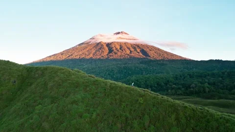 Lone Explorer Traversing Mountain Landscape Beneath Cloud Capped Volcano Peak Stock Footage 340322221