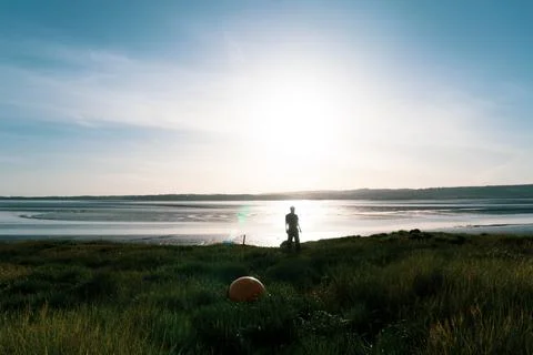 A lone figure, back with camera standing on the edge of an estuary. Stock Photos