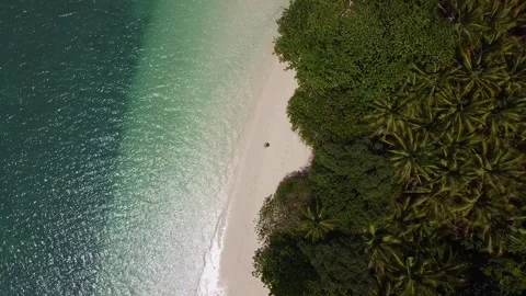 A lone figure sits on the sandy beach of a tropical island 库存影片 170608517