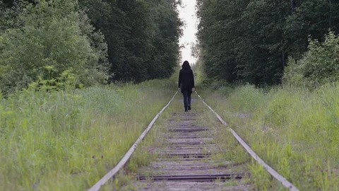 A lone guy in black is walking on the rails in the woods, back view. He feels Stock Footage 123045693