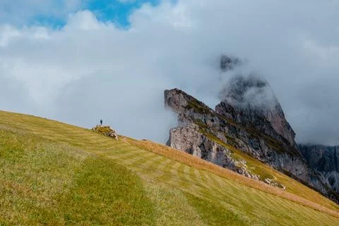 Lone hiker on grassy slope with dramatic Dolomites peaks shrouded in clouds Stock Photos