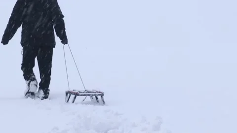 A lone man pulls a sleigh across a snowy field. A teenager travels in the win Stock Footage 165908243