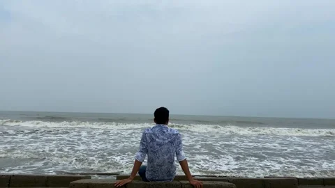 Lone man sitting on vast sea shore and watching ocean waves with sky - static Stock Footage 341870604