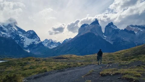 A lone man slowly walks toward the dramatic Cuernos del Paine mountains in Chile Stock Footage 335347386