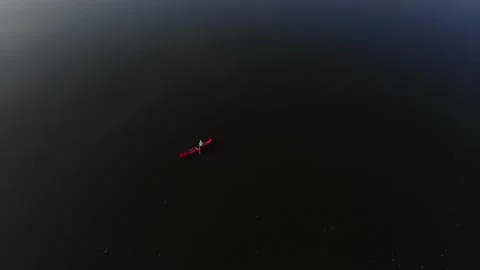 Lone person in red canoe rowing on dark lake during day Stock Footage 138762362