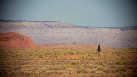 Lone rider in desert with cliffs in background Vídeo Stock 102265629