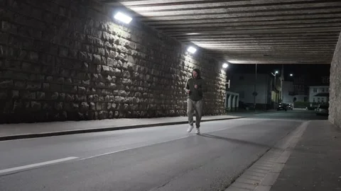 A lone runner swiftly moves through a dark urban underpass at night, displaying Stock Footage 309054199