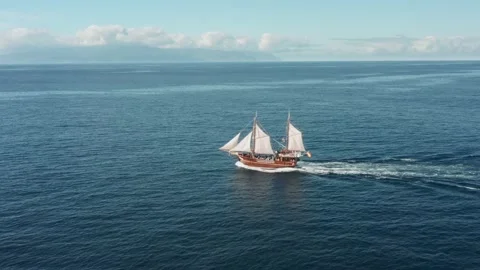 A lone sailboat with white sails glides over the waves on the open sea in clear 스톡 동영상 137414062