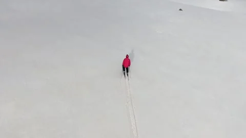 Lone skier crosses a flat snowfield in a red jacket - Flat White and Ski Route Stock Footage 339360904