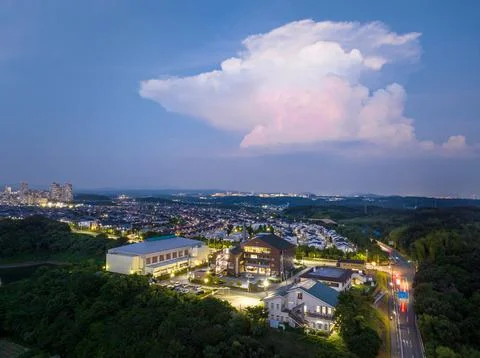 Lone towering cloud over bright buildings and suburban development at dusk Stock Photos