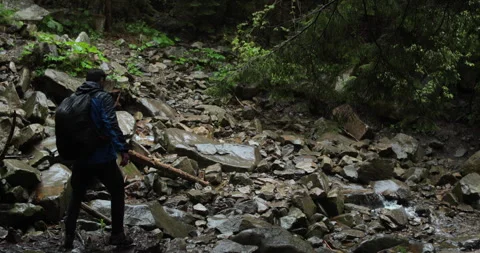 A lone traveler with a backpack and wearing a blue jacket is walking on rocky Stockbeeldmateriaal 243718482
