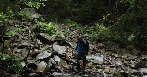 A lone traveler with a backpack and wearing a blue jacket is walking on rocky Stockbeeldmateriaal 243720871