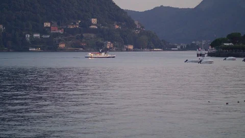 A lone white small ship floats on the blue surface of Lake Como in the evening Stock Footage 128427890