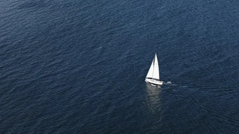 Lone yacht sails through expansive blue ocean in dramatic aerial view. Stock Footage 313342018