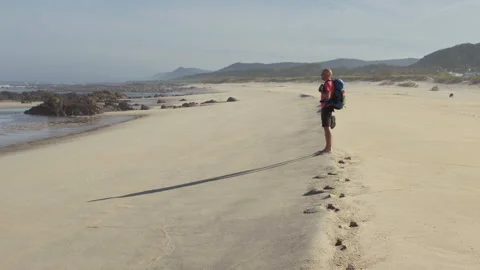 Lonely backpacker man walking along sandy beach washed by Atlantic Ocean waves 動画素材 330872506