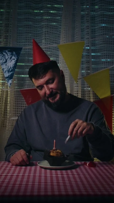 Lonely bearded man in a party hat puts out a cigarette in his birthday cupcake. Stock Footage 338406562