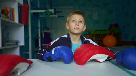 Lonely Boy in Boxing Gloves Sitting Alone and Looking Out Window Stock Footage 343781356
