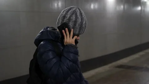Lonely boy in hat and jacket talking on phone in underground covered passage in Stock Footage 168096148