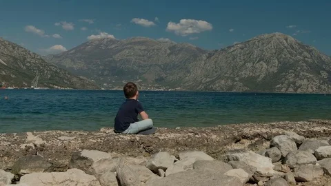 Lonely Boy Sitting against the background of the sea and mountains Stock Footage 74384509