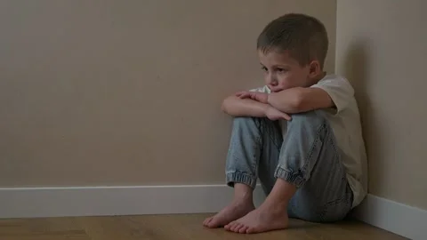Lonely boy sitting on floor in corner. Thinking deeply while holding knees tight Stock Footage 320113871