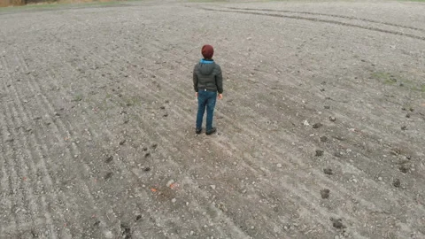 The lonely boy wanders in autumn in an empty, plowed, gray field. The croaker is Stock Footage 106528190