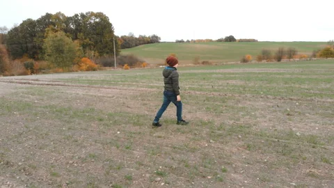 The lonely boy wanders in autumn in an empty, plowed, gray field.  Stock-Footage 136489656