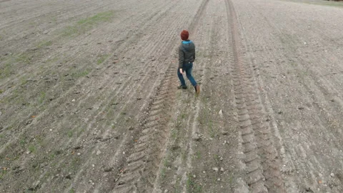 The lonely boy wanders in autumn in an empty, plowed, gray field.  Stock Footage 136490969