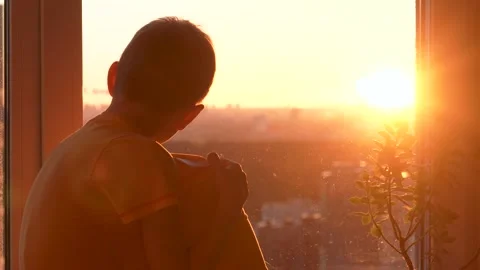 Lonely boy watching sunset through window sitting on windowsill Stock Footage 325212239