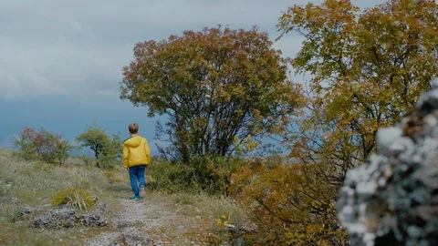 Lonely boy in a yellow jacket is walking along a path in nature. Stock Footage 111956407