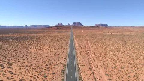 Lonely car driving along an empty straight road leading towards iconic mountains 動画素材 113648355